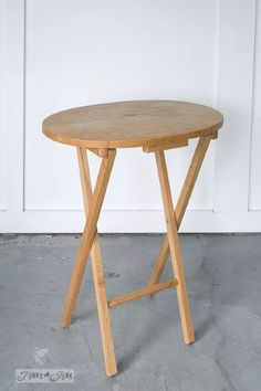 a small wooden table sitting on top of a cement floor next to a white wall