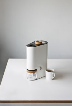 a white coffee maker next to a cup of coffee