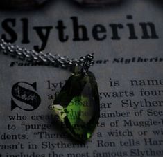 a green necklace sitting on top of an open book with the word slytherin written below it