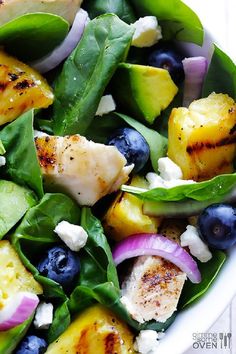 a salad with chicken, blueberries, cucumbers and spinach on it