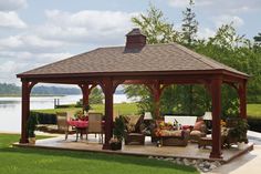 a wooden gazebo sitting on top of a lush green field next to a lake