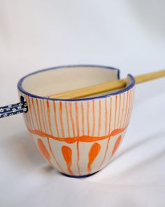 an orange and white bowl with chopsticks in it