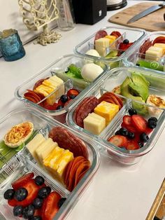 four plastic containers filled with assorted fruits and cheeses on top of a table