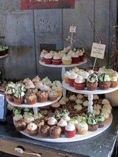 cupcakes are displayed on three tiered trays in front of a sign