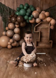 a baby sitting on top of a cake in front of some balloons and other decorations