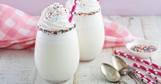 two glasses filled with white frosting and sprinkles next to spoons