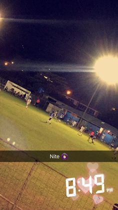 people are playing soccer on a field at night with the scoreboard lit up in front of them