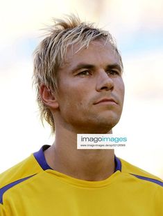 a man with blonde hair wearing a yellow soccer uniform looking off to the side while holding a soccer ball in his hand