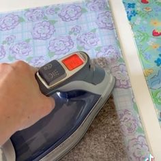 a person using an iron on top of a sheet of fabric next to a flowered table cloth