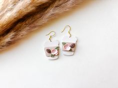 a pair of earrings with pink flowers on them sitting next to a furry animal's tail