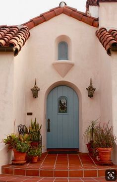 a blue door is on the side of a white stucco building with potted plants