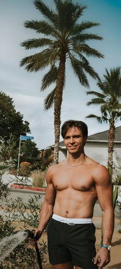 a shirtless man holding a surfboard in front of palm trees