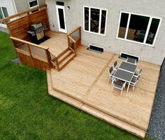 a wooden deck with table and chairs next to a house