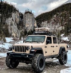 a beige jeep parked on top of a snow covered slope next to trees and mountains