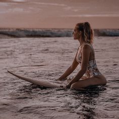 a woman is sitting on her surfboard in the water at sunset or dawn,