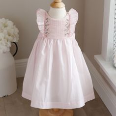 This Little Dress By Luli & Me Is Super Sweet! The Pale Pink Dress Is Done In A Cotton Blend For Easy Care And Less Wrinkles. The Bodice Is Done In A Pinafore Style With Ruffles Starting At The Waist And Extending Over The Shoulder To The Back. The Ruffle Is Edges With A Contrasting Pink Embroidery, The Center Of The Bodice Has A Horizontal Accordion Smocking. To The Edges Are Vertical, Two-Toned Pink Chevron Borders With Hand Embroidered Flowers Done In Hues Of Blue, Pink, And Lavender. The Lar Spring Dress With Smocked Bodice For Playdate, Sleeveless Dress With Smocked Back For Playdate, Spring Smocked Dress For Playdate, Summer Dress With Smocked Bodice For Playdate, Pink Smocked Dress For Summer Playtime, Pink Smocked Dress For Playtime In Summer, Cute Smocked Dress For Dress-up, Pink Smocked Bodice Dress For Dress-up, Pink Smocked Bodice Dress For Playdate