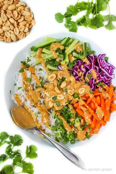 a white plate topped with rice and veggies covered in peanut sauce next to a bowl of cashews