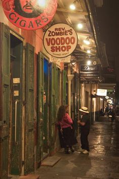 two people are walking down the sidewalk in front of some shops at night time,