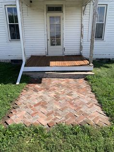 a small white house with a brick walkway leading up to the front door and porch