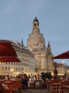 people sitting at tables in front of an old building with a clock tower on top