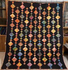 a black quilt with orange, yellow and blue designs hanging from it's center