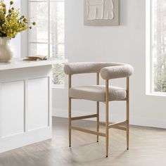 a white chair sitting in front of a window next to a vase filled with flowers