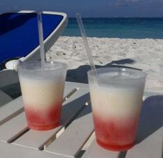 two drinks sitting on top of a table next to the ocean