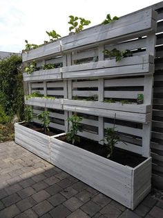 a wooden planter filled with plants sitting on top of a brick floor next to a fence