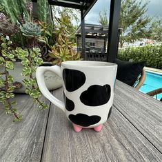 a black and white polka dot coffee mug sitting on a wooden table next to a pool