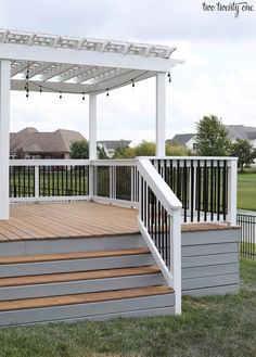 a white pergolan sitting on top of a wooden deck next to a green field