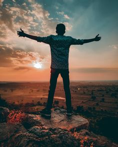 a man standing on top of a rock with his arms outstretched in front of the sun