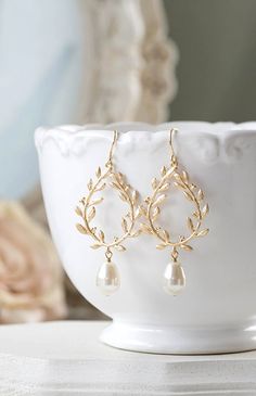 a pair of gold - plated earrings with white pearls and leaves on the side