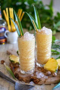 two glasses filled with drinks sitting on top of a wooden table next to some plants