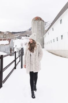 a woman walking through the snow in front of a silo with a hat on