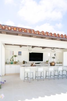 an outdoor kitchen with bar stools and a television mounted on the wall above it