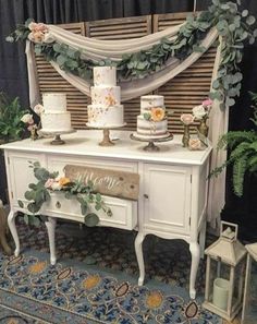 a white table topped with lots of cakes and greenery next to a blue rug