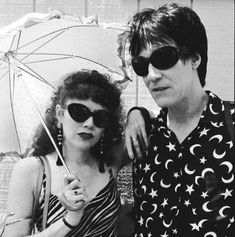 two people standing next to each other with an umbrella over their heads and sun glasses on