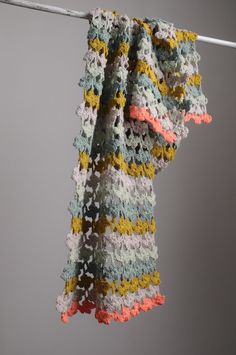 a multicolored crocheted scarf hanging on a clothes line against a gray background