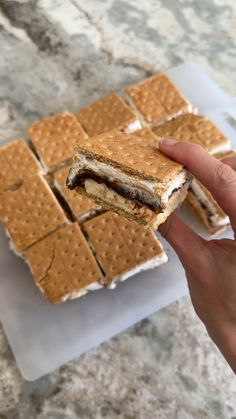 a person is holding up a sandwich with graham crackers on the table next to them