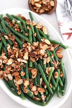 green beans with walnuts and almonds in a white bowl on top of a table