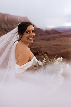 a woman in a wedding dress holding a bouquet with veil over her head and smiling at the camera