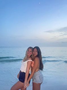 two girls standing on the beach with their arms around each other