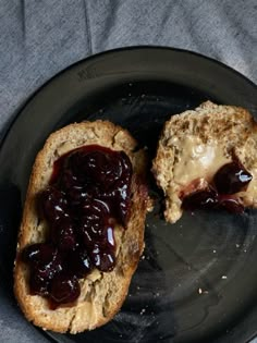 two pieces of bread with jam on them sitting on a black plate next to a gray cloth