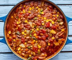 a blue pot filled with stew and vegetables on top of a wooden table next to a spoon