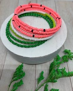 four bracelets are sitting on top of a white plate with green and pink beads