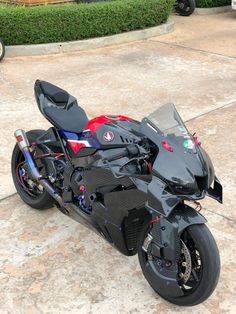 a black motorcycle parked on top of a cement floor next to a lush green bush