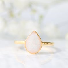 a gold ring with a white opal in the middle and flowers in the background