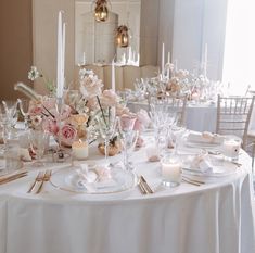 the table is set with white and pink flowers, silverware, candles and napkins