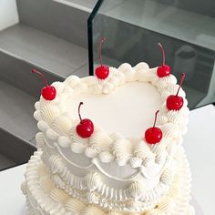 a heart - shaped cake with cherries on top sits on a table next to some stairs