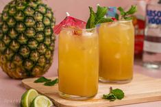 two glasses filled with drinks next to a pineapple on a cutting board and some limes